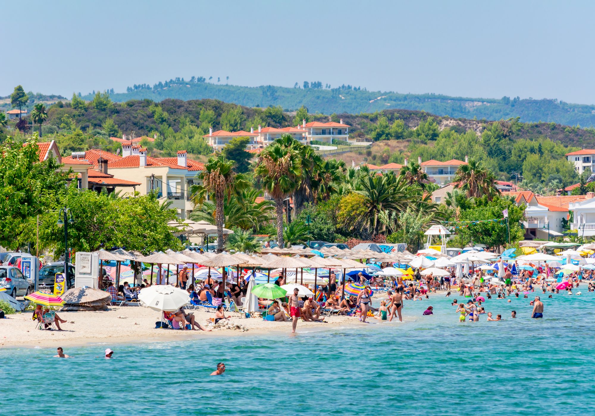 Mange badegæster på den dejlige strand i Pefkohori, med udsigt til byen og det frodige, grønne landskab på Halkidiki, Grækenland.