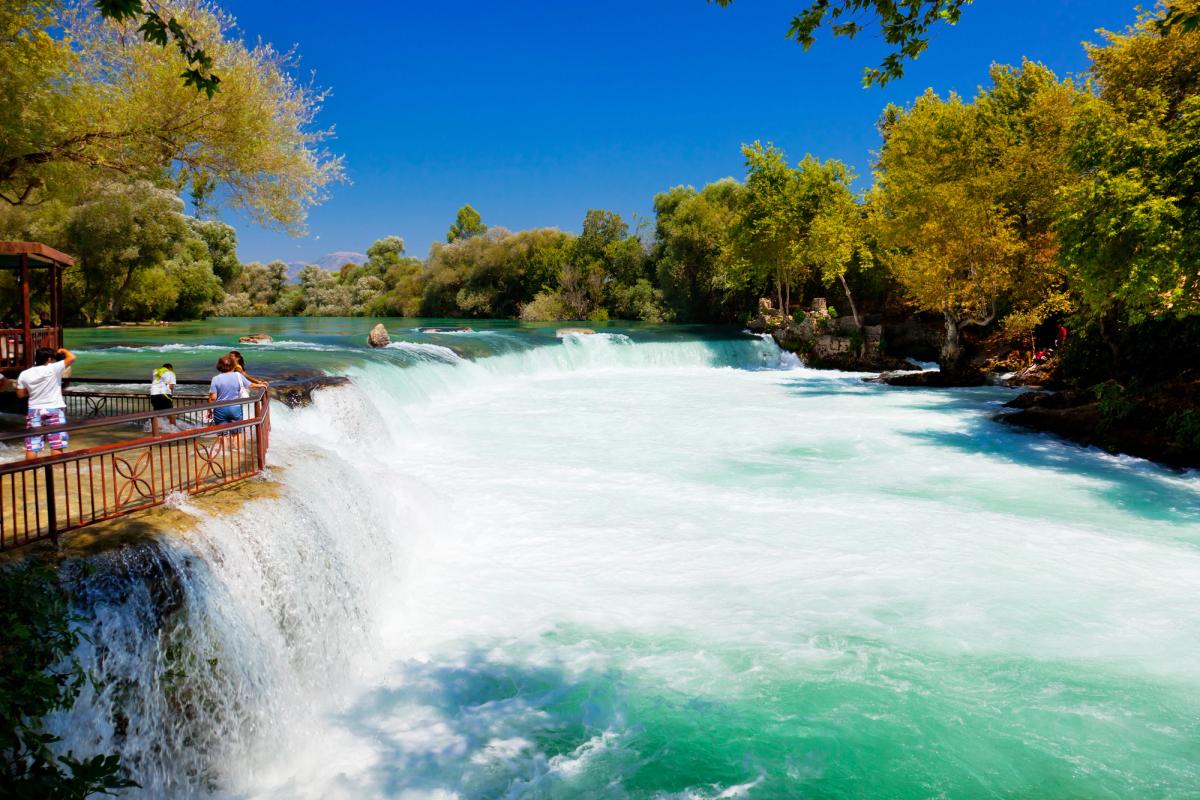 Fossefallene ved Manavgat. Til venstre i bildet en terrasse med enkelte turister som ser utover de brede fossefallene. Omkranset av høy skog.