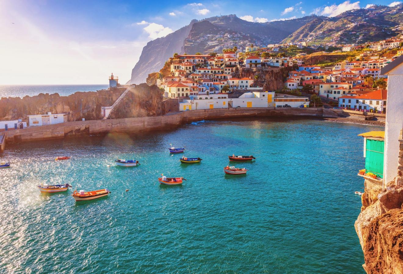 En vik på Madeira, in mot en mindre fiskeby. I vattnet ligger flera små fiskebåtar. Viken är omgiven av låg bebyggelse och området bakom är en frodig och sluttande bergsformation