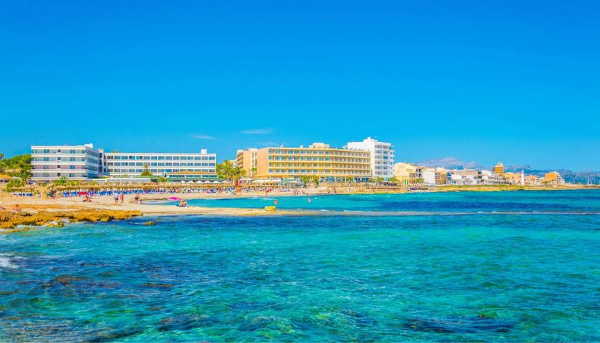 Byen Can Picafort sett fra sjøen. Her ser du først det krystallklare vannet som går over til bystranden i Can Picafort med hotellbebyggelse i bakgrunnen