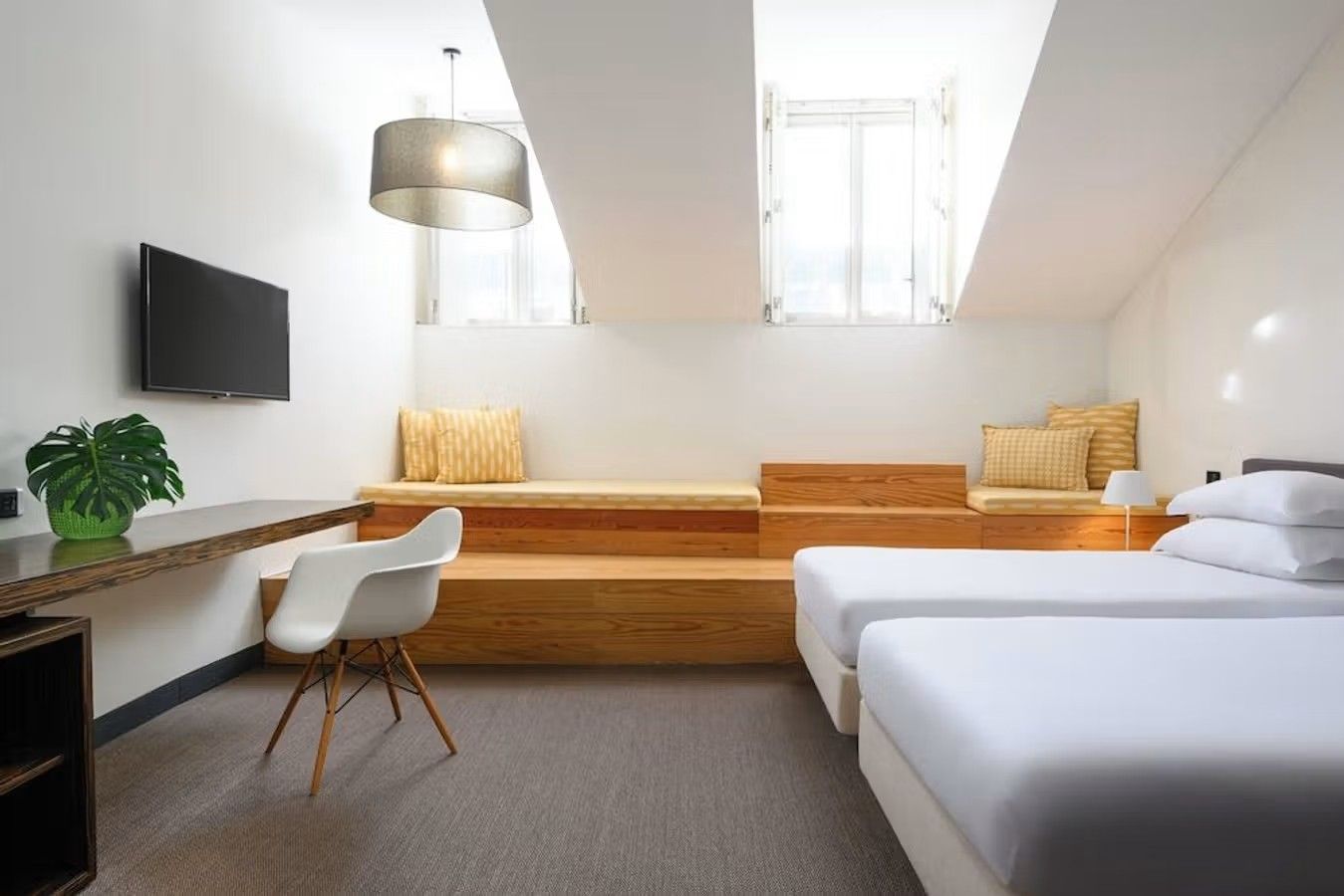 Et hotellrom med to hvite senger og en "trappesats" under to takvinduer som gir masse lys i rommet.
