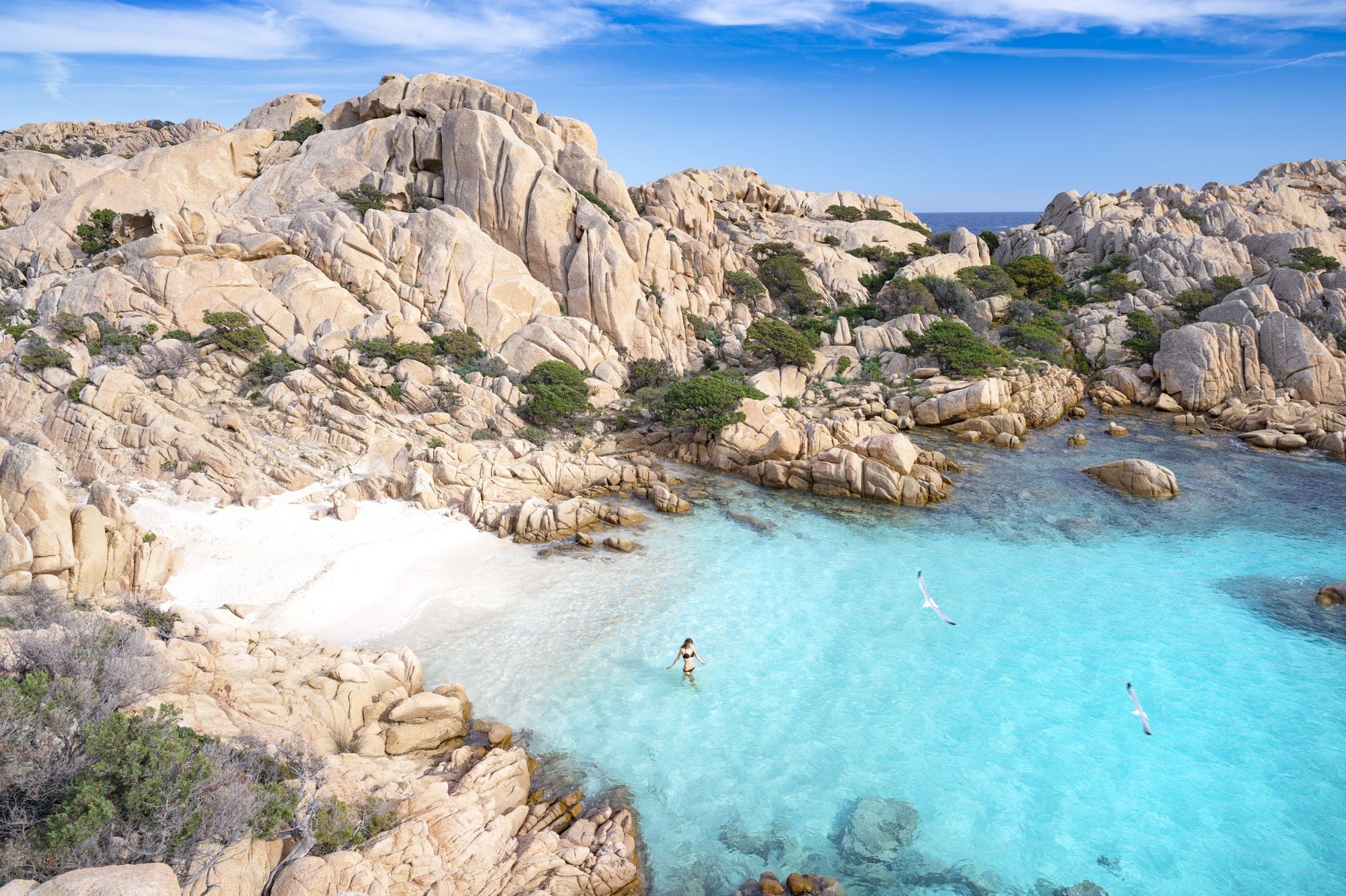 En smal strand med turkos färg, omgiven av klippor, vid Madallena på Sardinien i Italien