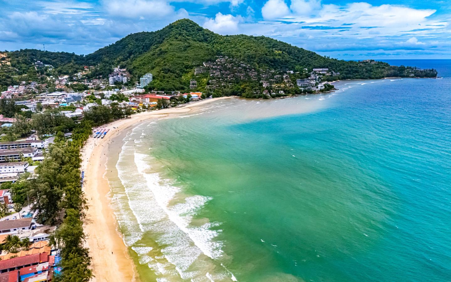 Udsigt over Kamala Beach med azurblåt hav og grønne bakker på Phuket i Thailand.