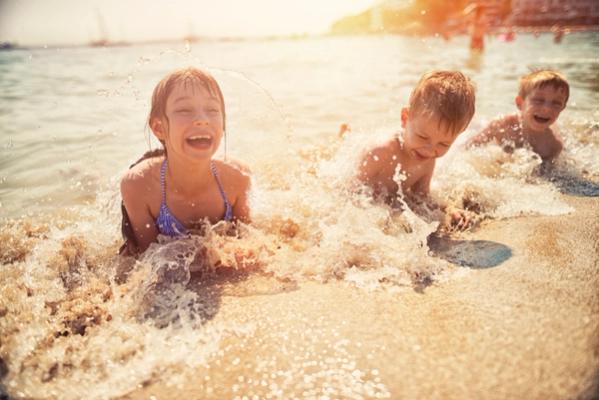 3 små børn leger i vandkanten på en lavvandet strand