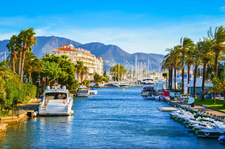 Båthavn i Empuriabrava med rekke på rekke av fortøyde fritidsbåter, omgitt av kanaler og moderne bebyggelse under en klar blå himmel – en idyllisk scene fra den unike kystbyen ved Middelhavet i Catalonia, Spania