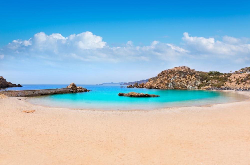 Usikt over Cala Cortina stranden ved Cartagena, en bred sandstrand i en bukt rundt ett klart grønnblått hav i Murcia-regionen