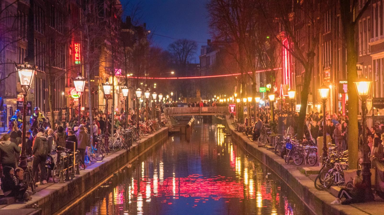 Billedet viser nattelivet i Red Light District om aftenen med den klassiske røde belysning langs og på tværs af kanalerne