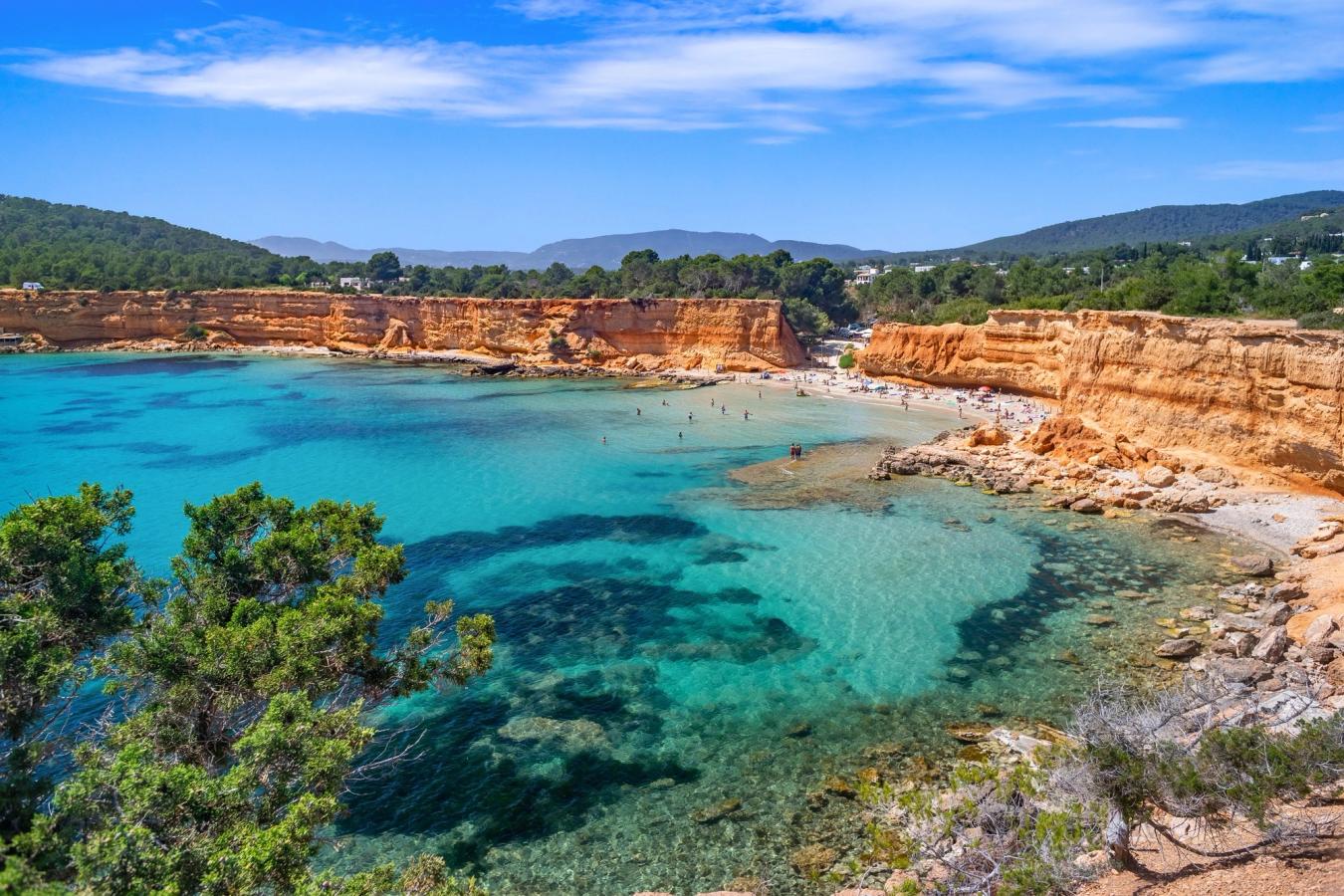 Bilde av stranden og bukta Es Bol Nou på sydspissen av Ibiza. Med sine rødfargede klipper rett bak det turkisgrønne vannet og stranden
