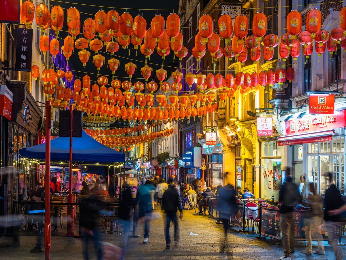 Bilden är från kvällstid i Chinatown i London. Vi ser en bilfri gata med ett antal människor som promenerar mellan olika restauranger och matställen på vardera sidan av gatan. Bord, stolar och olika reklamskyltar präglar gatubilden. Klassiska asiatiska röda papperslampor hänger ovanför gatan