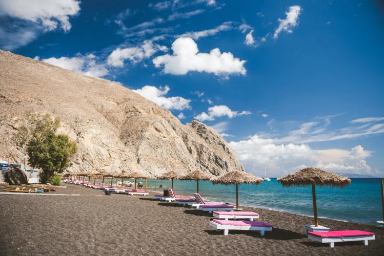 Utsikt over stranden med solstoler og klippene i Perissa på Santorini 