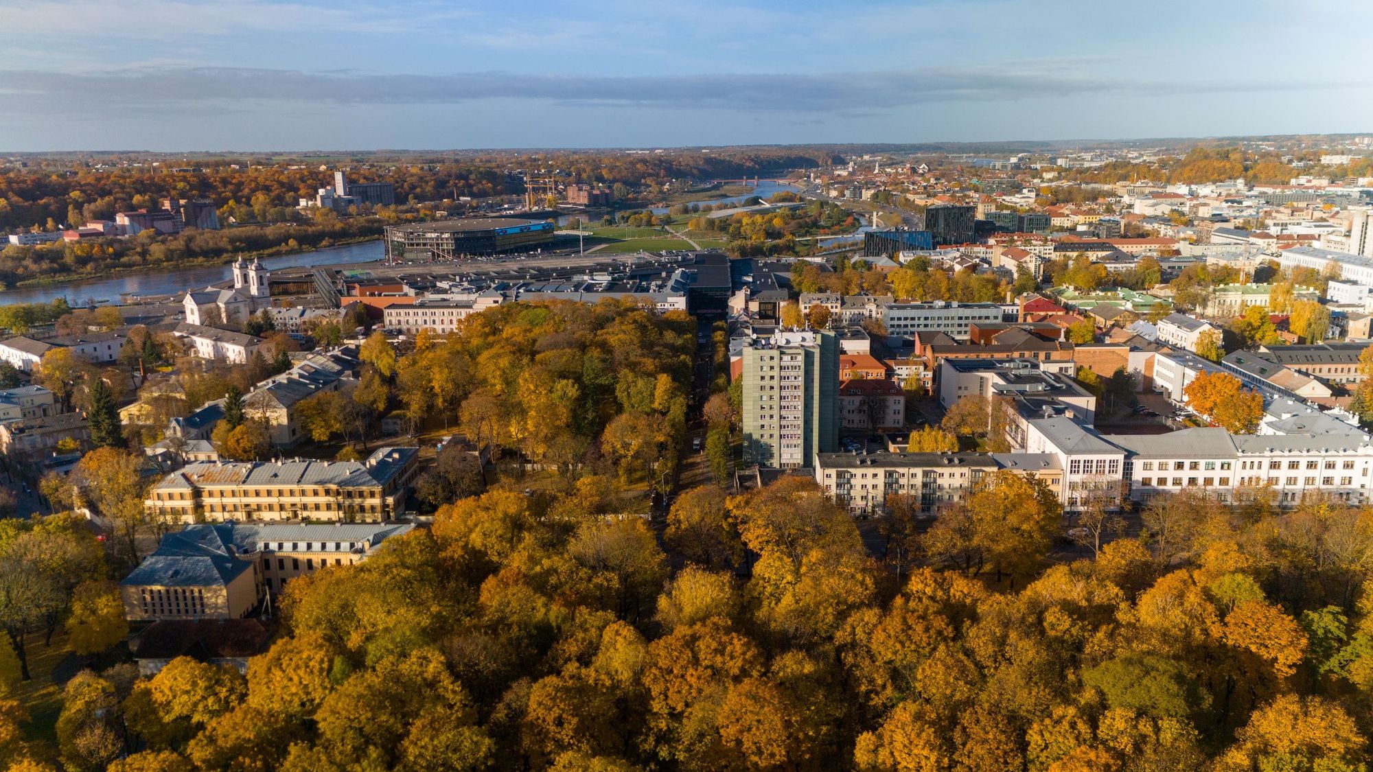 Kaunas i efterårsfarver med gyldne træer, byens nye bydel, boligblokke og Zalgiris Arena ved floden Nemunas i baggrunden.
