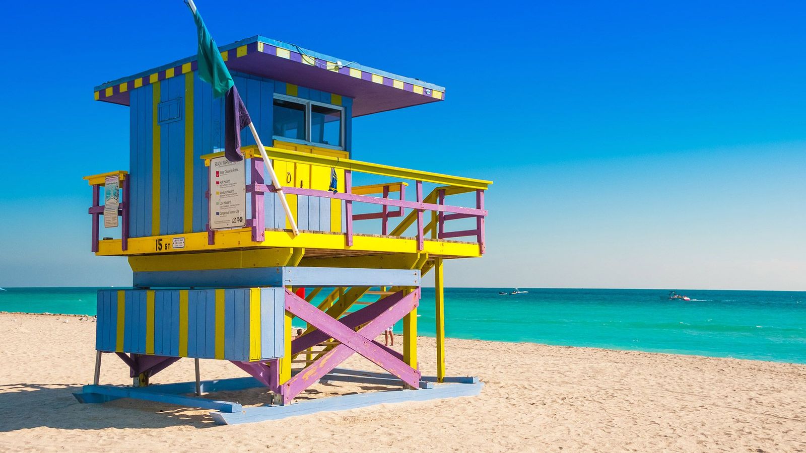 Fargerikt livreddertårn i pastellfarger på South Beach i Miami. Det står på den lyse sandstranden med turkisblått hav i bakgrunnen og en klar blå himmel over.