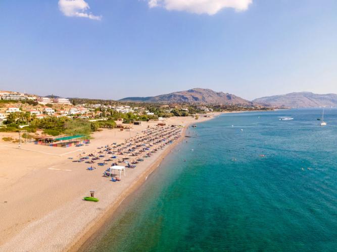 Bildet viser den lange og langgrunne stranda i Kiotari. Høyre side av bildet det stillestående og krystallklare vannet med stranda og solparasoller til venstre.