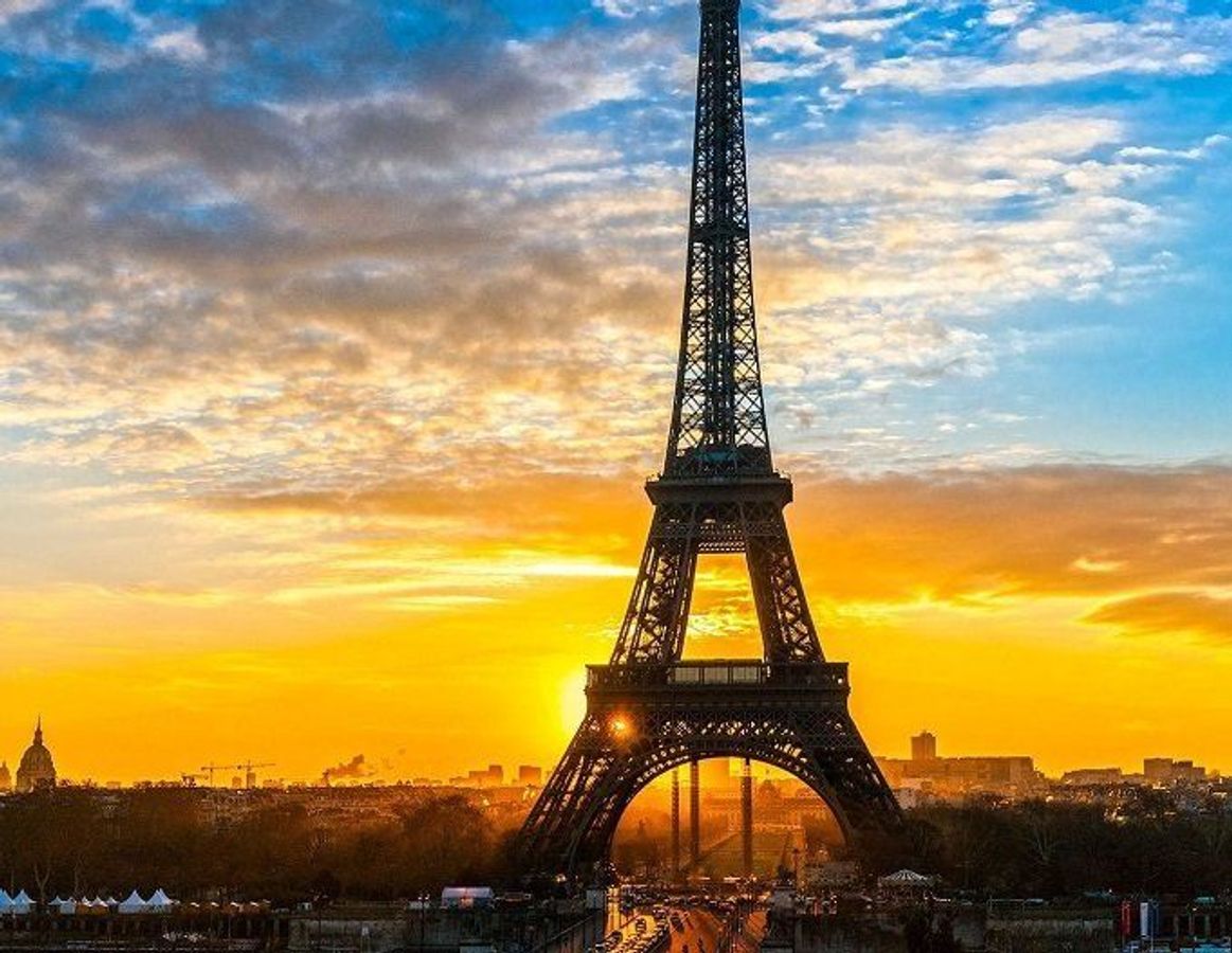 Billedet viser Eiffeltårnet i solnedgang med en blanding af orange og blå himmel i baggrunden