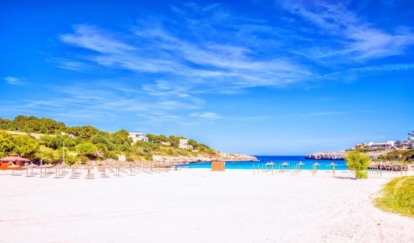 På bilden ses en vit strand med parasoller och det turkosblå Medelhavet i bakgrunden