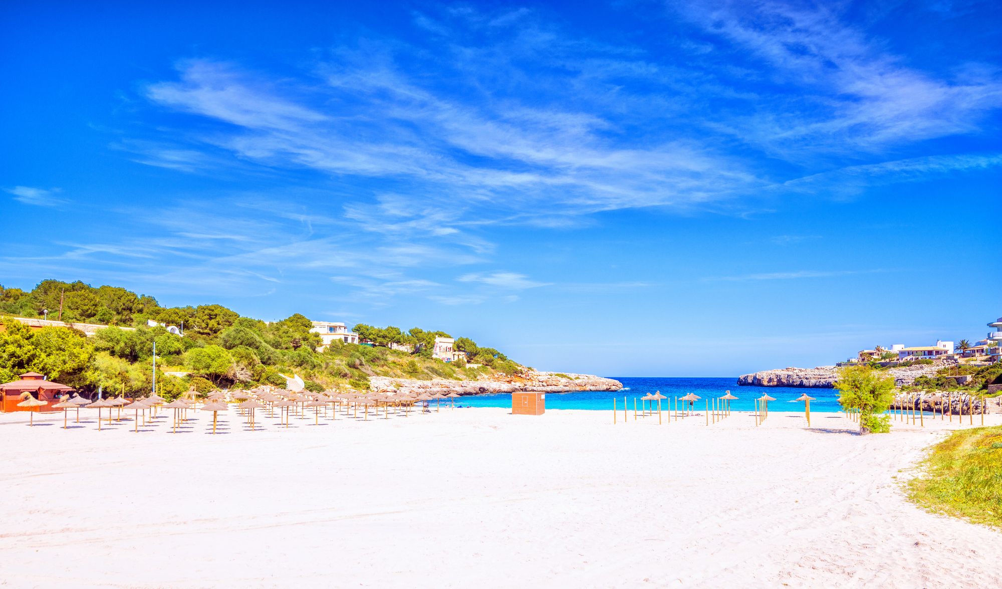 På bildet sees en hvit strand med parasoller og det turkisblå Middelhavet i bakgrunnen