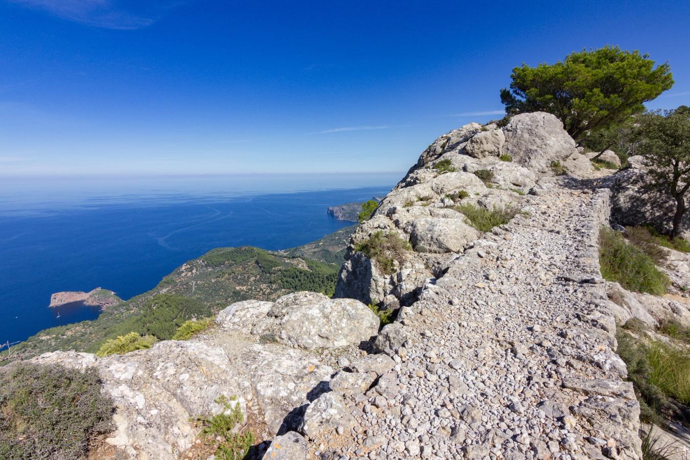 Langs en fjellside går en liten sti med utsikt over Middelhavet og landskapet. 
