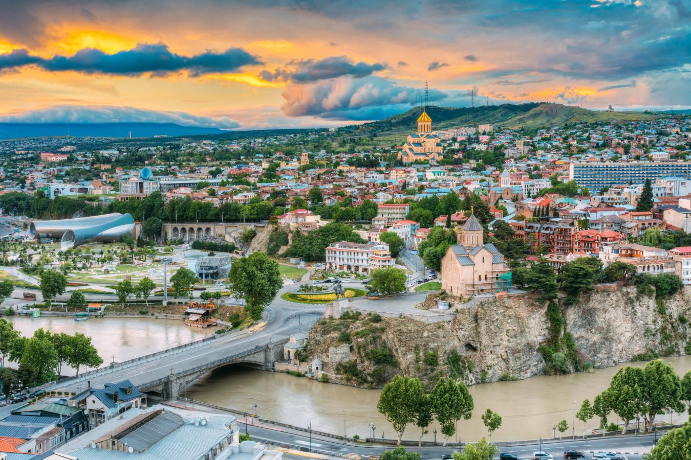 Aftenbillede over Tbilisi, hvor vi til venstre i billedet ser den nye koncertsal og lige bagved Presidential Administration of Georgia med sin blå kuppel. Helt tæt på til højre, lige over floden, ser vi Metekhi-kirken, og midt i billedet længst inde ses Holy Trinity Cathedral of Tbilisi.