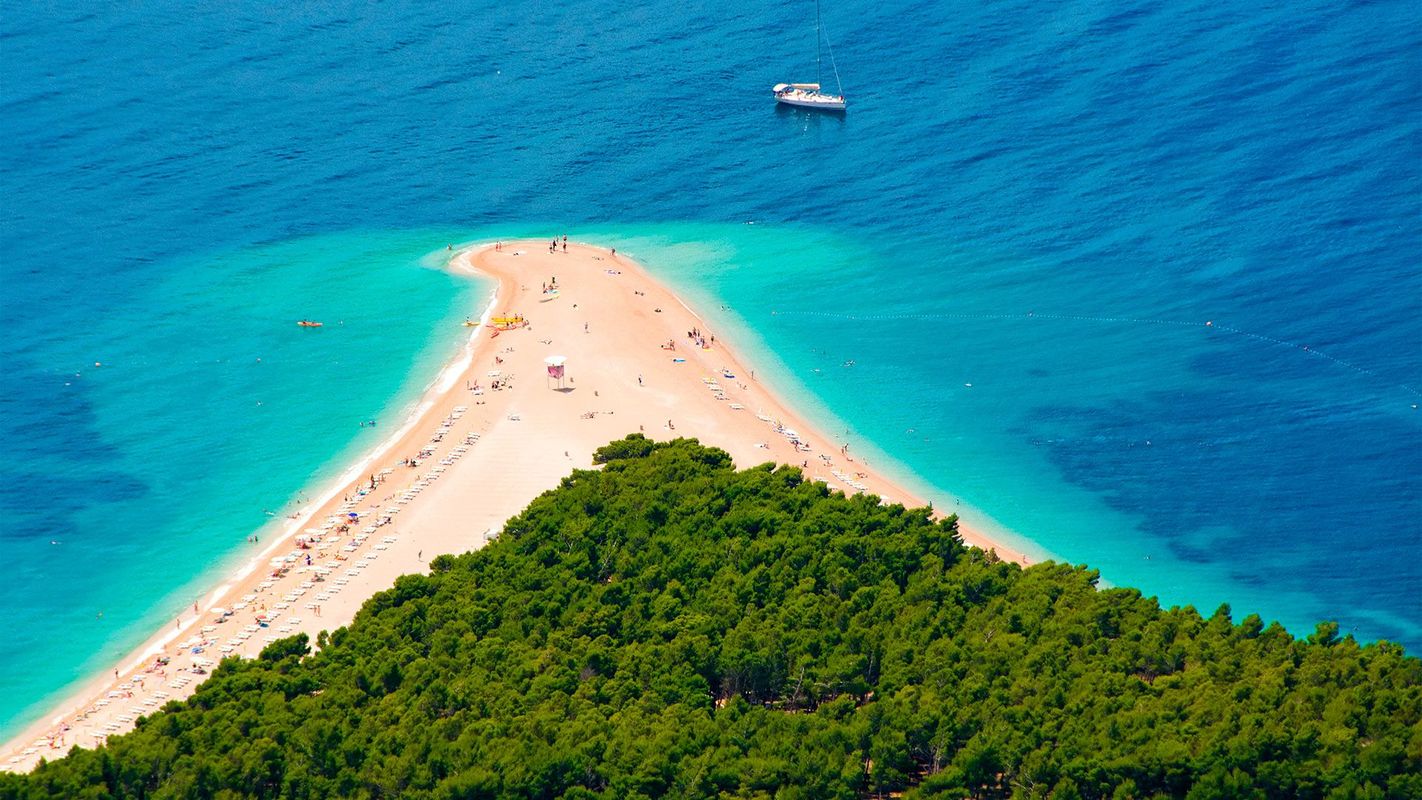 Utsikt från pinjeskogen över Zlatni Rat – den berömda landtungan vid Bol, omgiven av kristallklart, blått hav.