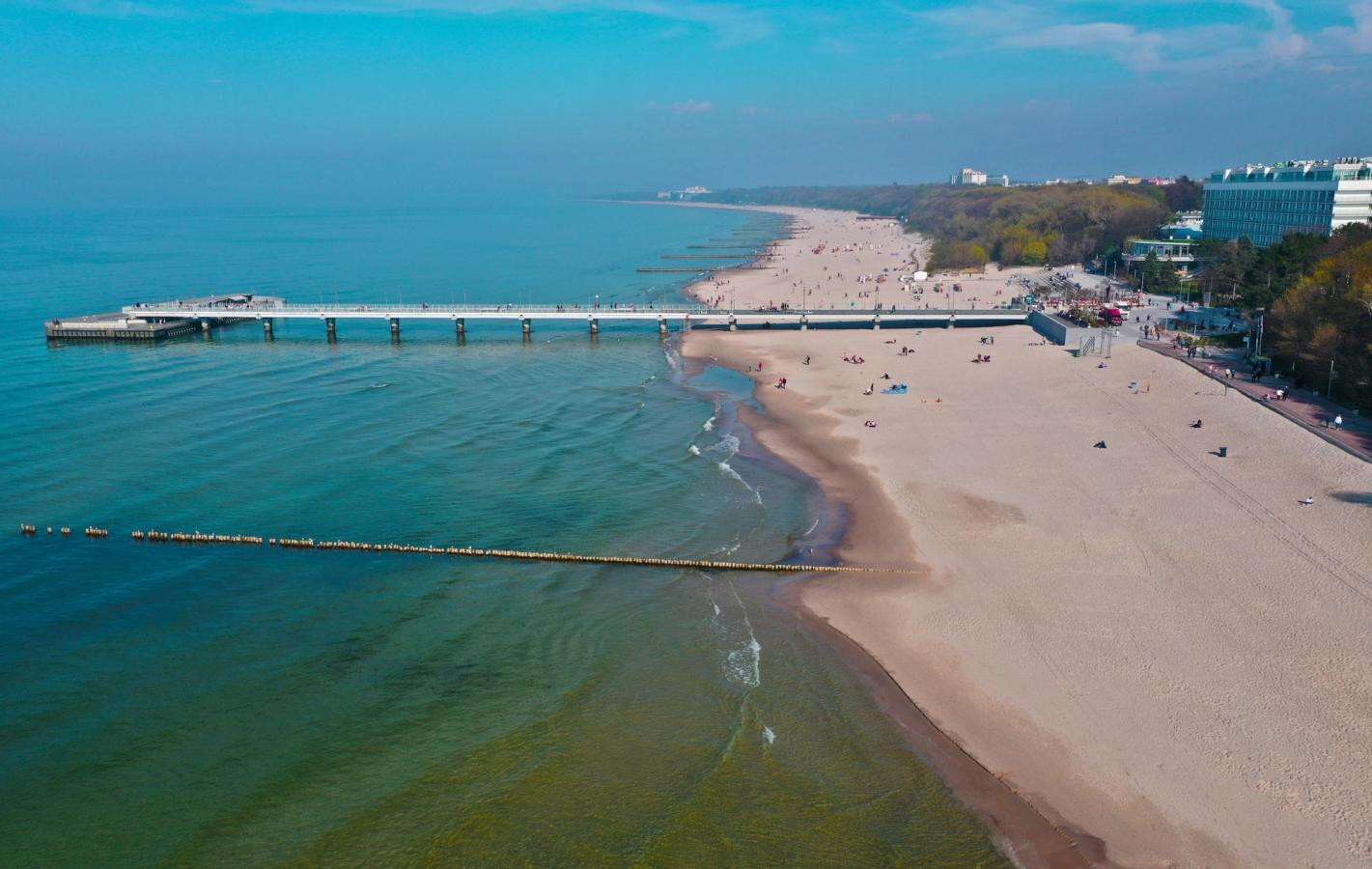 Billedet viser den næsten "endeløse" strand i Kolobrzeg og Østersøen. Med træmolen midt i billedet, der strækker sig langt ud i havet. Blå og skyfri himmel.