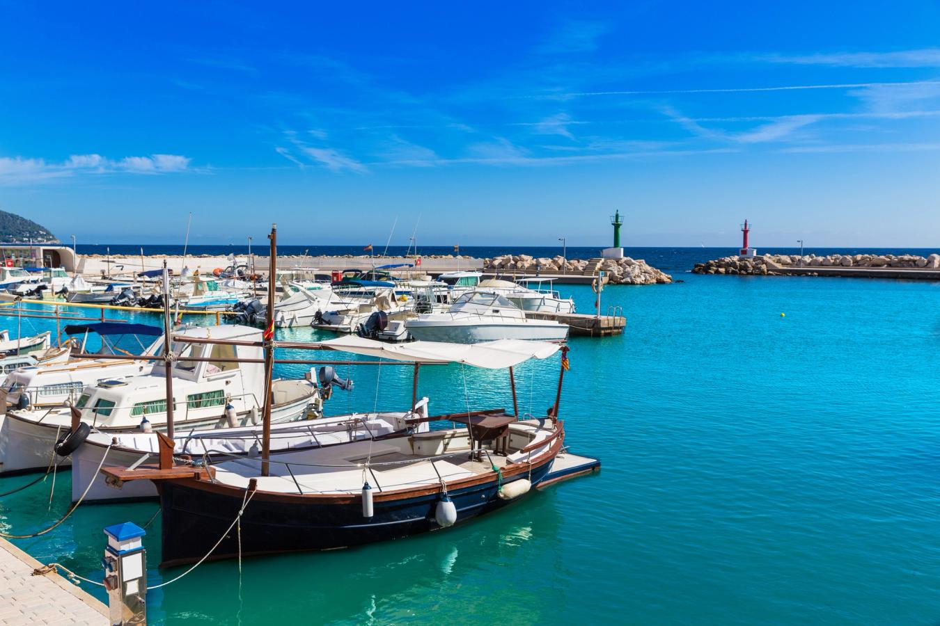Små fiskebåtar i hamnen i Cala Bona med turkosgrönt hav och ljusblå himmel i bakgrunden