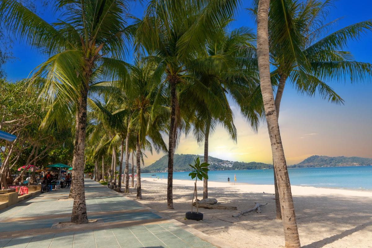 Strandpromenaden i Patong Beach med palmer och den vita sandstranden i solnedgången