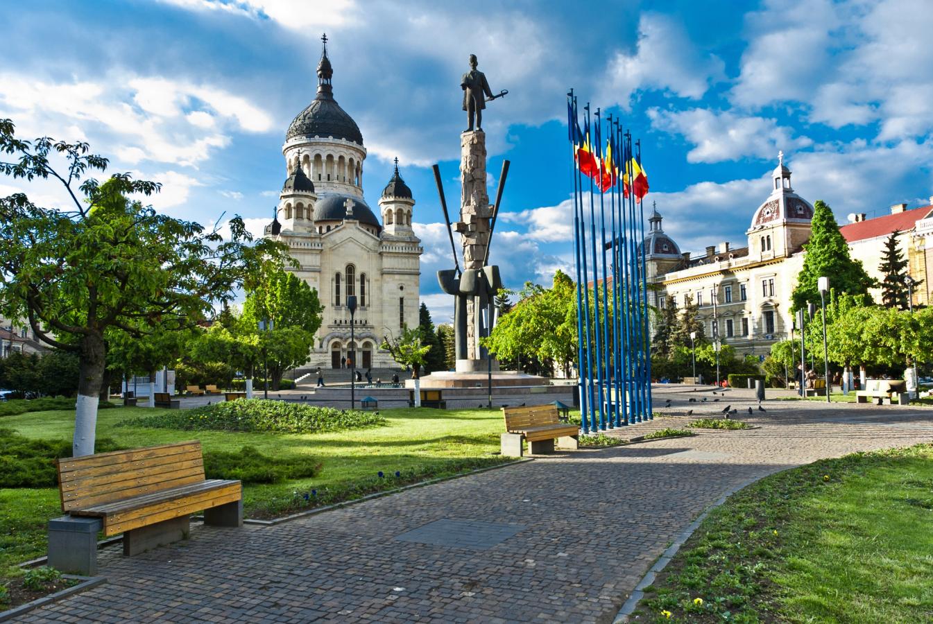 Torg i Cluj-Napoca med en stor katedral, ett högt monument och rumänska flaggor