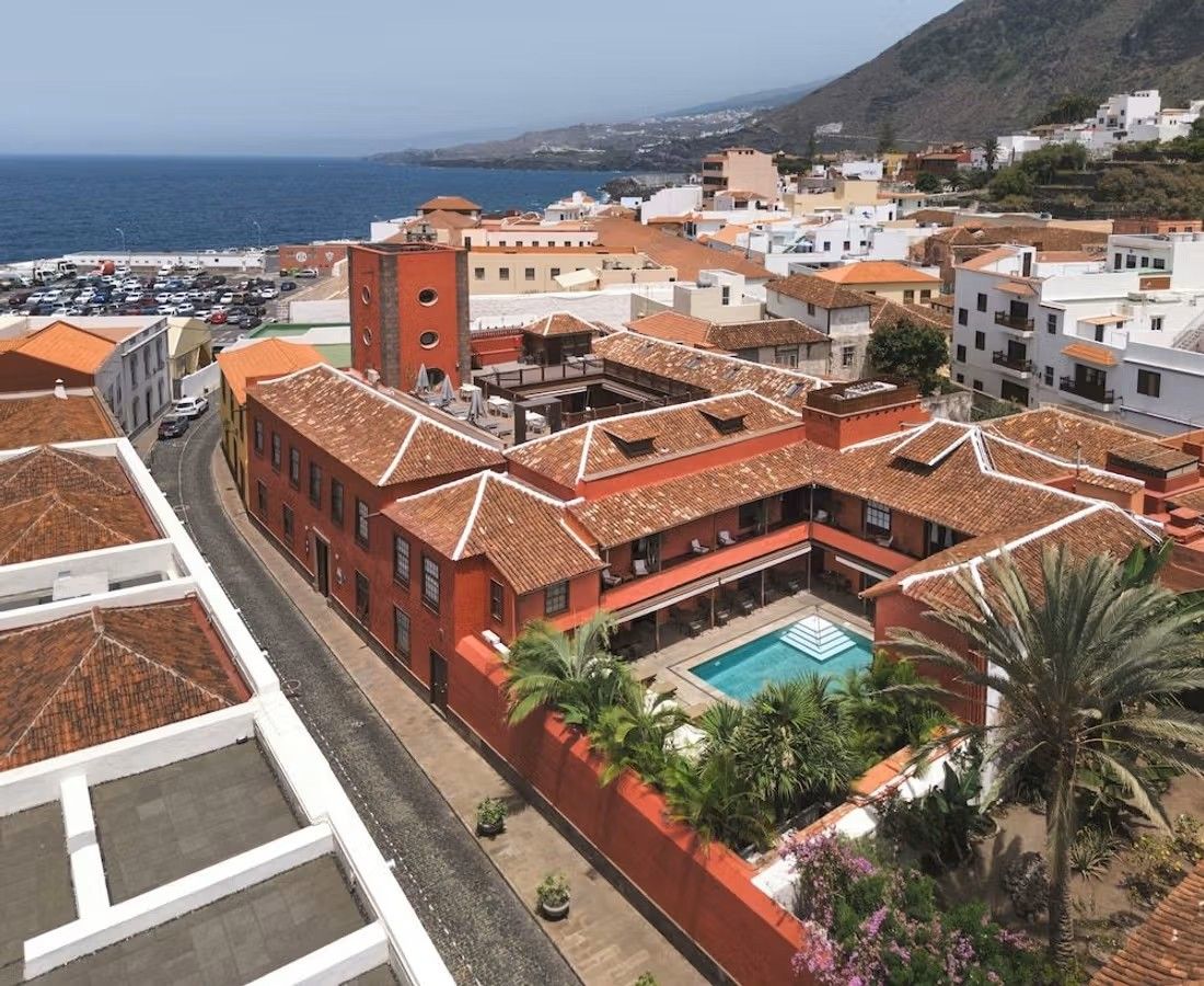 Bilde av Hotel San Roque i Garachico på Tenerife. Hotellet er en eldre herregård i rustrød farge. I bakgrunnen ser vi havet og starten på en klippevegg. Hotellet er delvis omgitt av hvit bebyggelse.