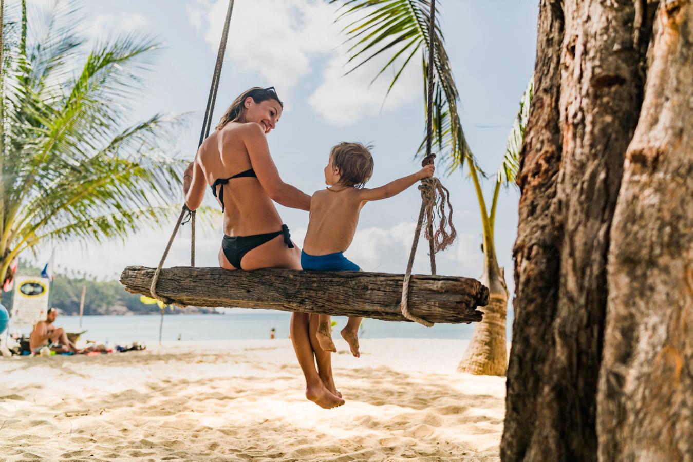 En mamma och hennes barn kopplar av en stund under palmerna på en vit sandstrand i Thailand