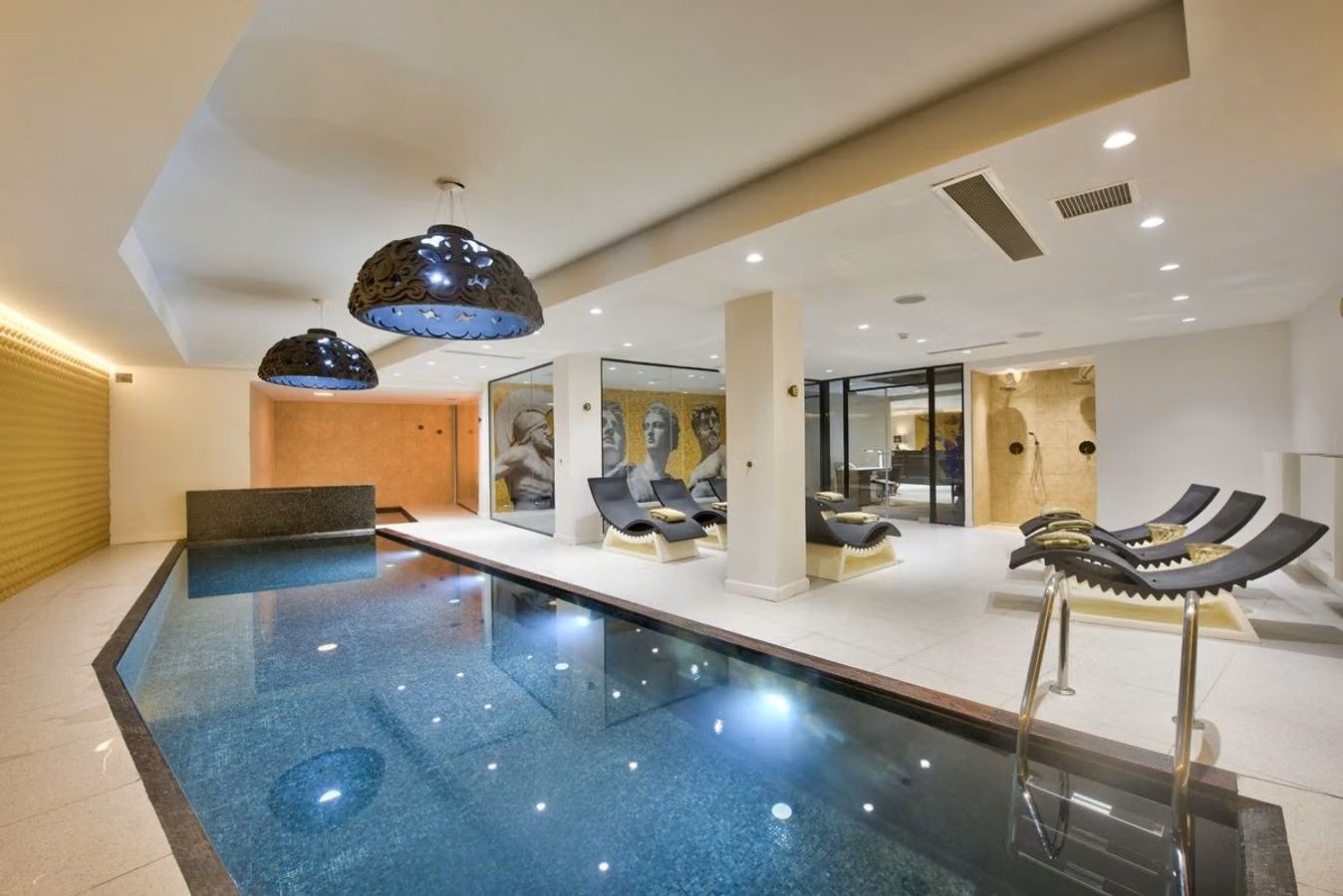 Bilden visar en mindre inomhuspool på hotellet Holm Boutique Spa i St. Julian's på Malta. Ovanför poolen hänger två stora lampor och det finns sittgrupper runtomkring.