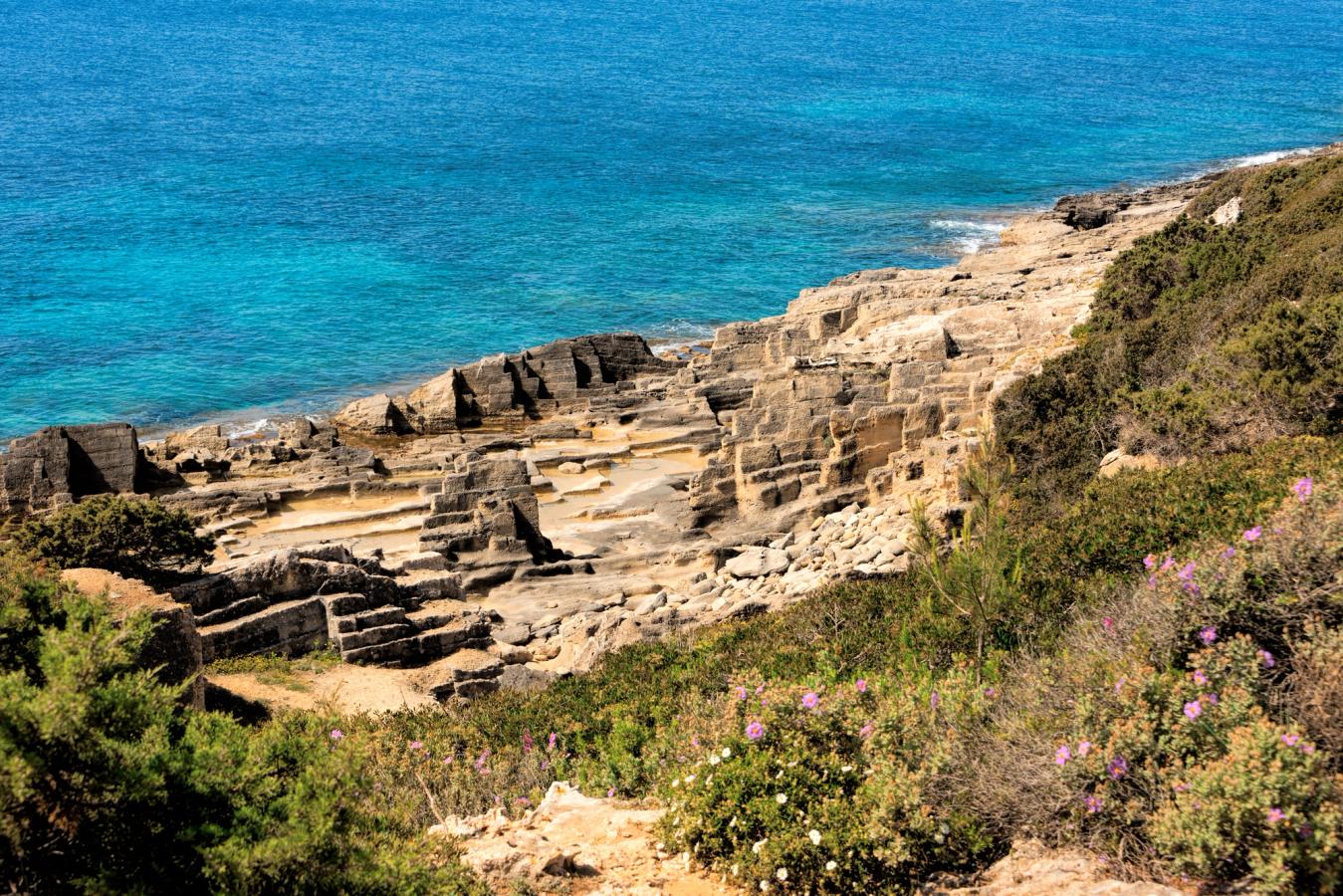Naturreservatet Punta de n'Amer på Mallorca. Klippor smälter samman med grön vegetation på en sluttning ner mot det kristallklara havet