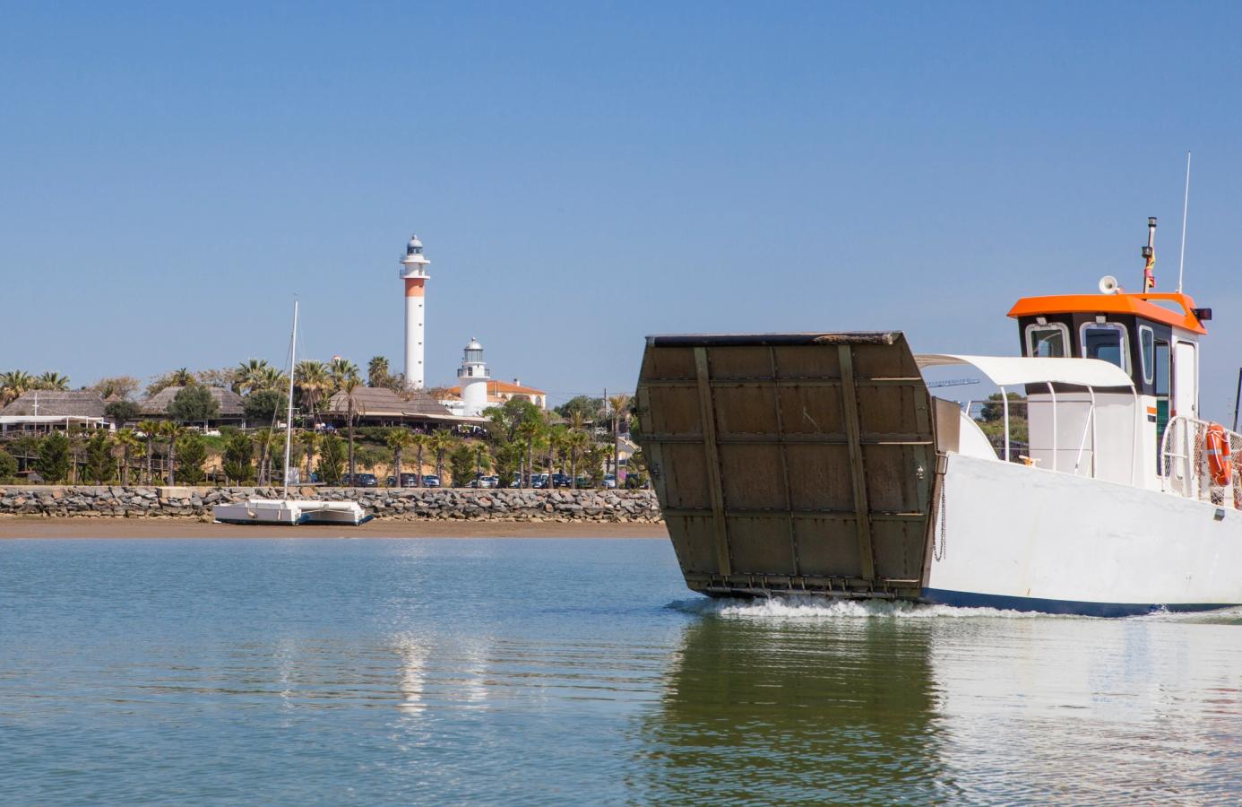 Bildet viser en båt som seiler fra havnen i El Rompido med de to kjente fyrtårnene i bakgrunnen. 