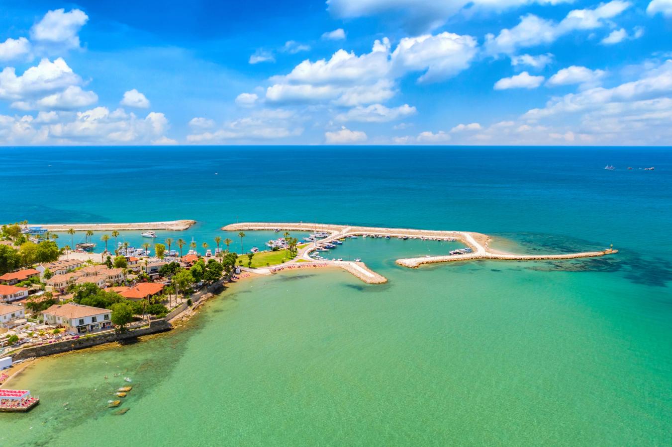 Billedet viser de smukke omgivelser i Side langs Antalya-kysten i Tyrkiet. Lav bebyggelse omgivet af moler, der giver roligt vand og turkisgrønne farver.