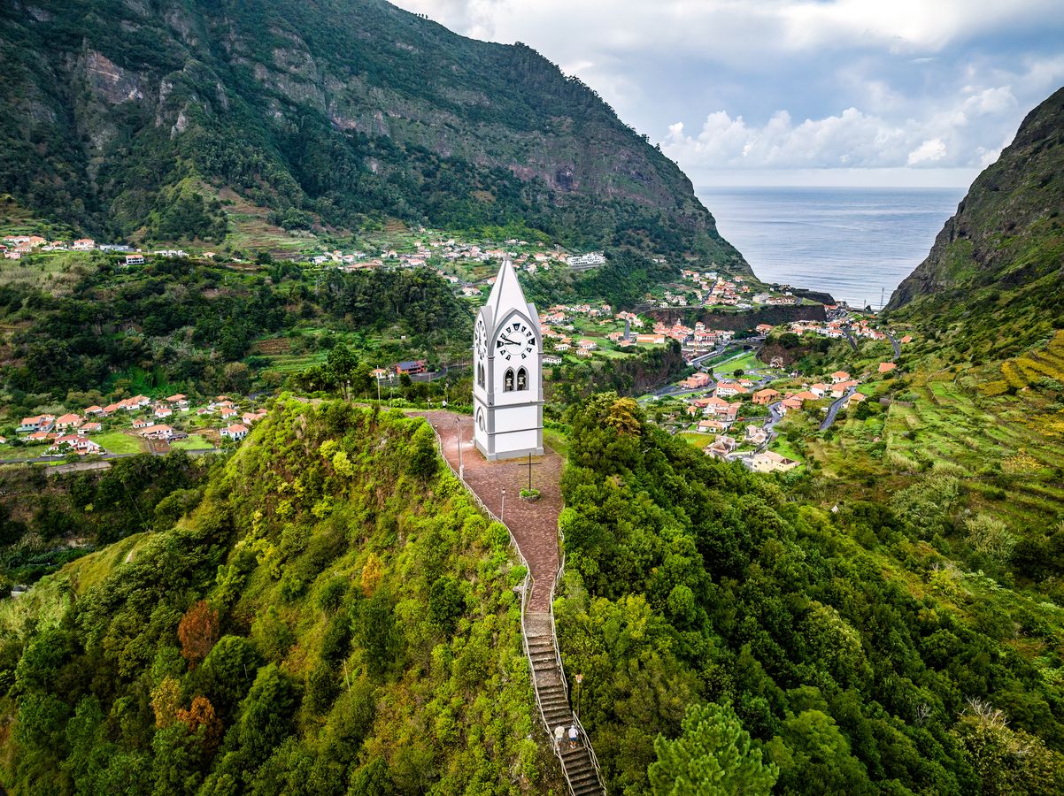 Billedet viser kapellet "Chapel of Our Lady of Fatima", som ligger på en lille bakketop omgivet af en frodig vegetation. Længere inde i billedet ser vi landsbyen Sao Vicente med stejle klippevægge på hver side. I midten og længst inde ender billedet i Atlanterhavet.