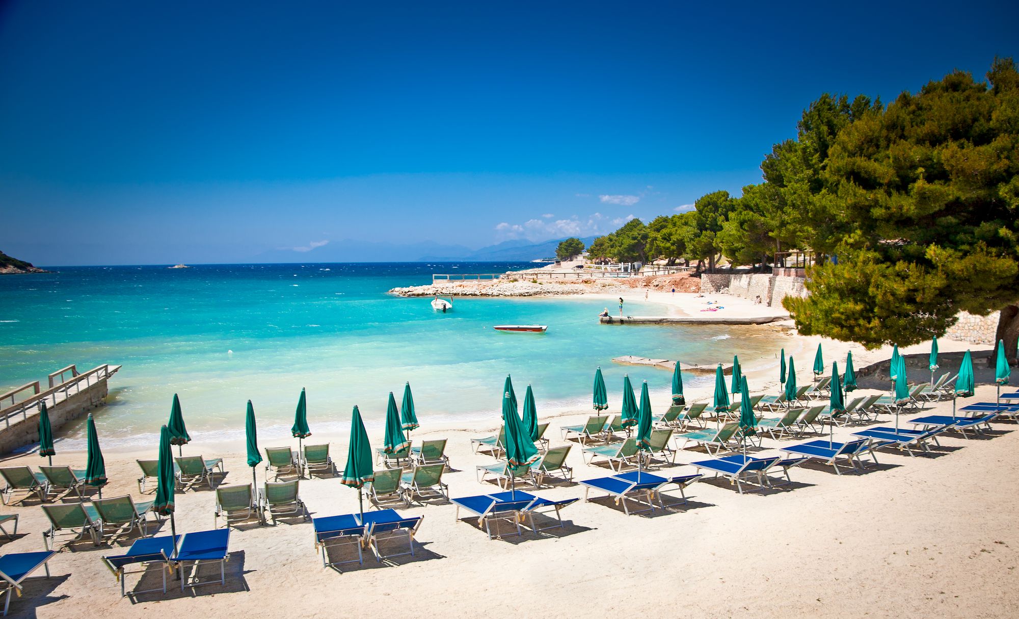 Blikkstille og turkis hav under en skyfri himmel på den kritthvite stranden i Ksamil i Albania