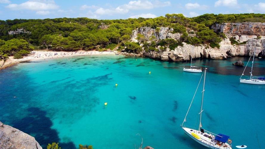 Udsigt over det turkise hav med sejlbåde og den idylliske strand Cala Macarella på Menorca i Spanien