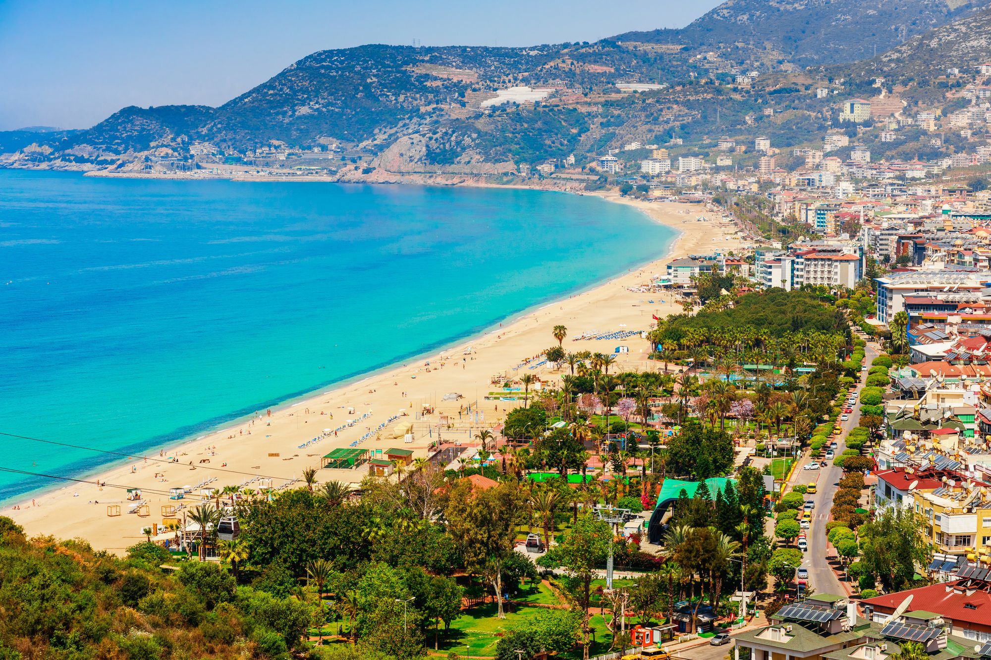 Utsikt över den långa, vita Kleopatra-stranden med turkosblått hav och gröna kullar vid horisonten i Alanya på Antalyakusten i Turkiet