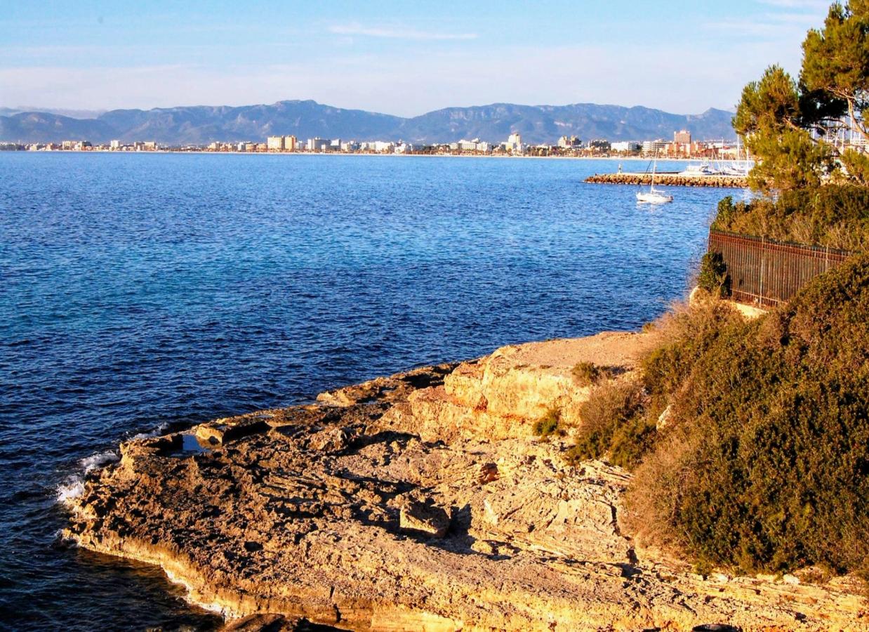 Det blå hav slår ind mod en klippeside. I baggrunden ser man byen. 