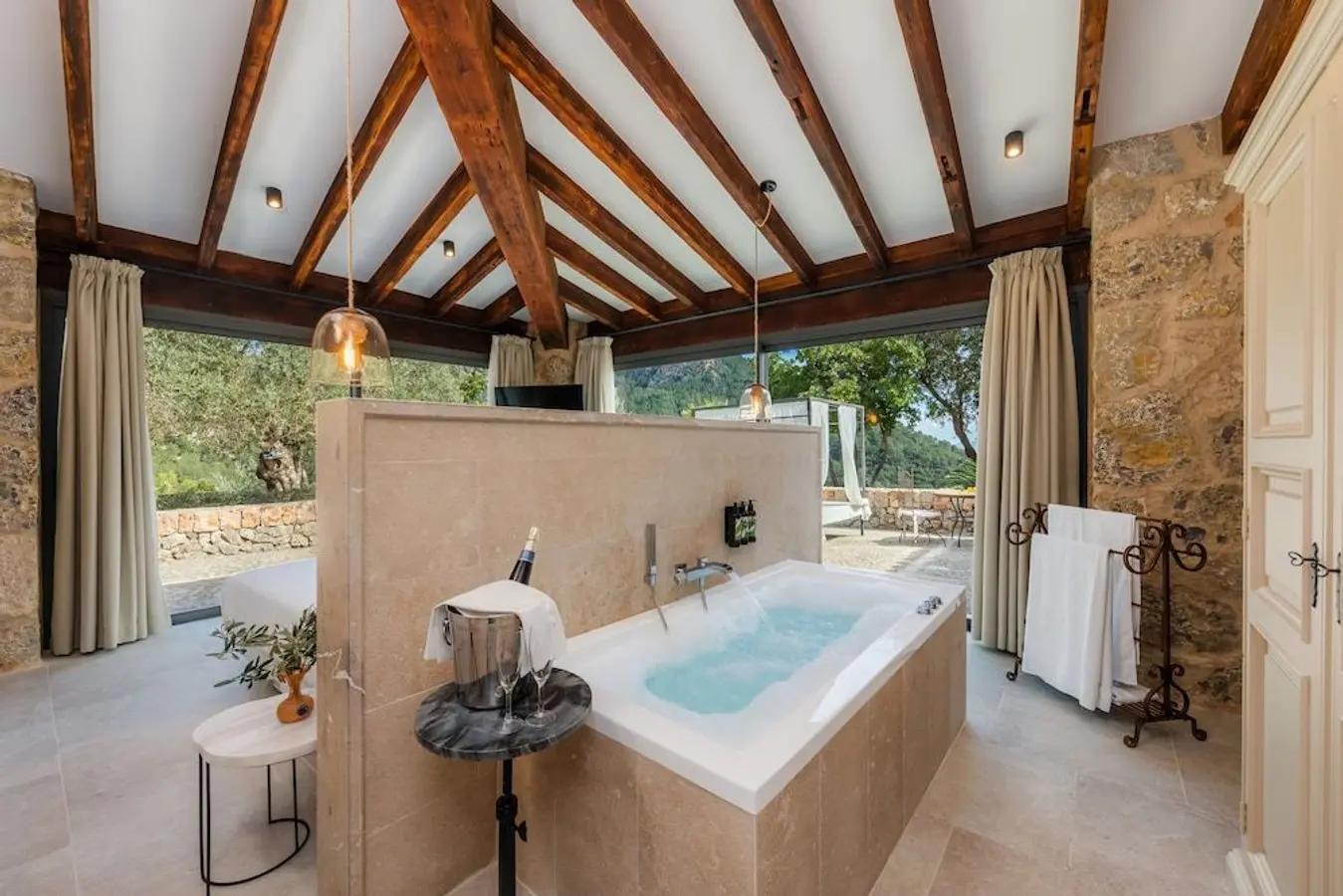 Bilden är från insidan av hotellet Finca Albellons. Stenväggar med ett öppet badrum och träbjälkar i taket. Med badkar och dubbelsäng i det öppna rummet där man precis utanför kan gå ut på en egen terrass.