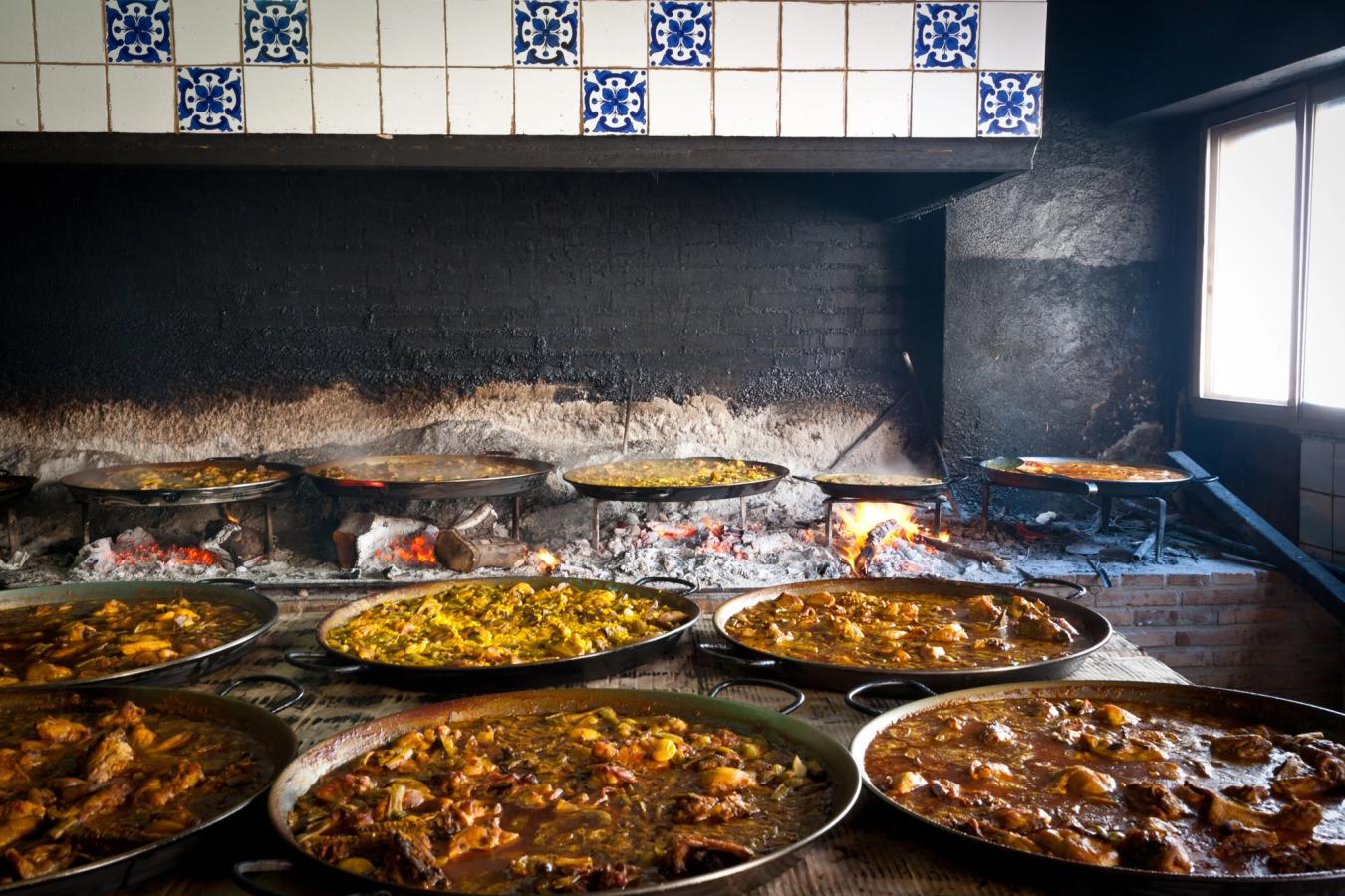 Bilden visar hur man på lokalt vis tillagar paella, ursprungligen från Valencia-regionen, över glödande träkol.