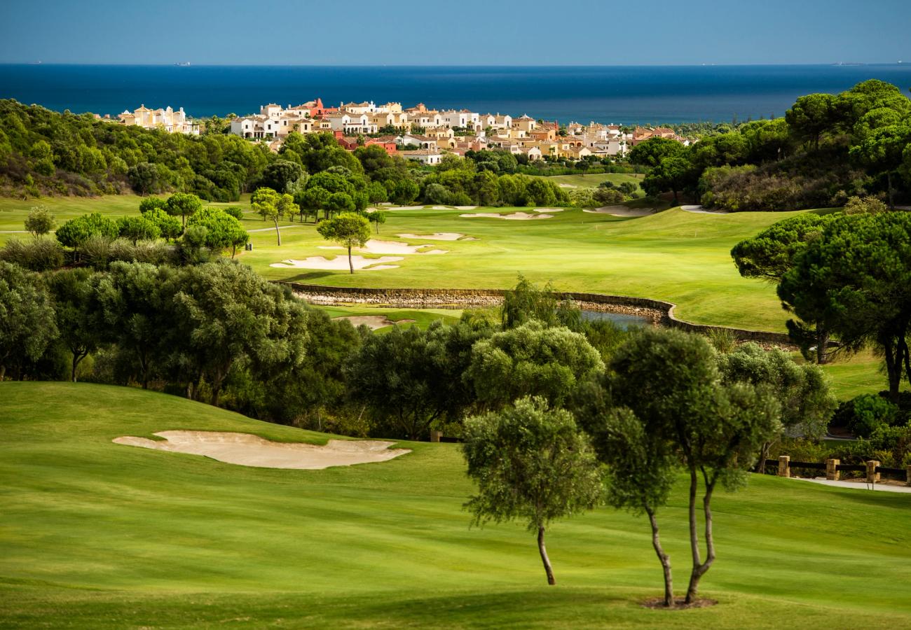 Utsikt over en grønn golfbane med noe vegetasjon og sandhull i Sotogrande på Costa del Sol. Lengst inn i bildet skimter man Middelhavet.