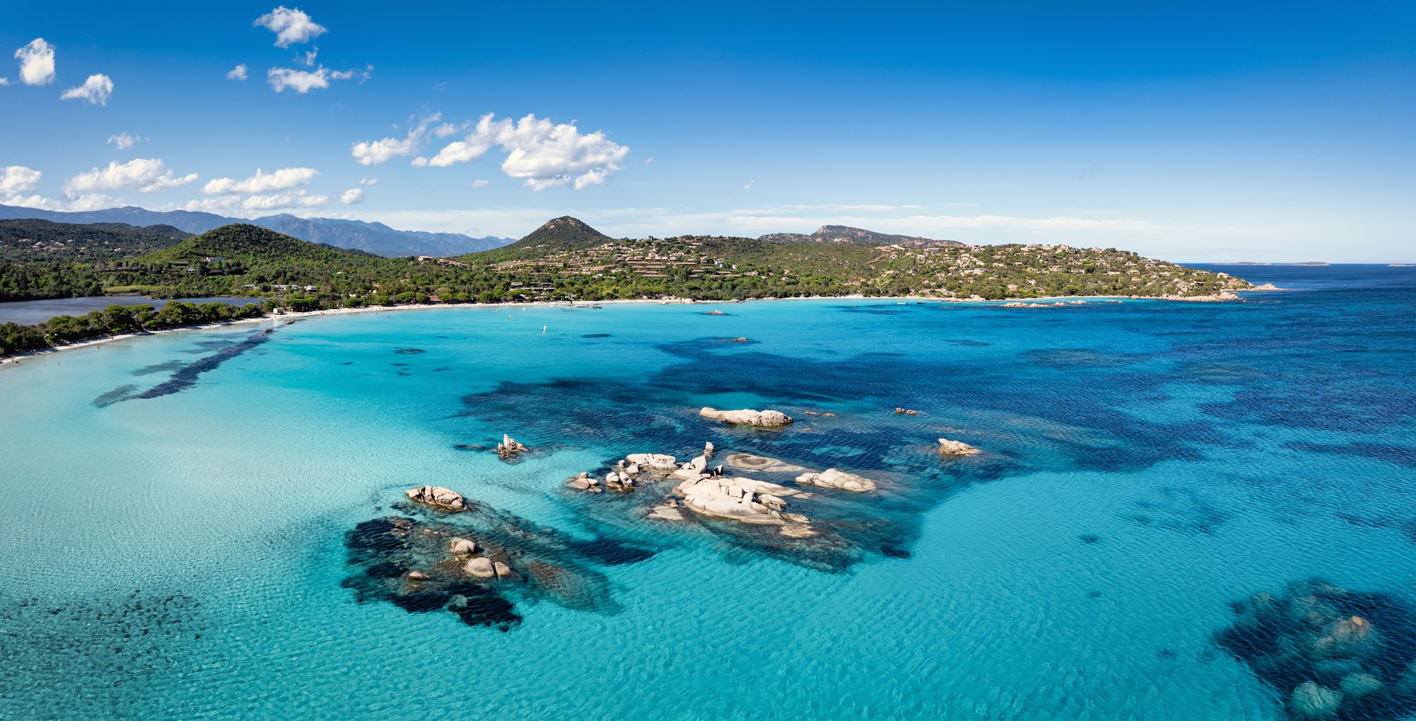 Panoramaudsigt over Santa Giulia Beach på Korsika. Billedet viser et blåt, roligt hav med et bakket og frodigt landskab i baggrunden.