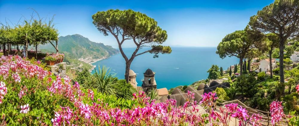 Utsikt over kysten i Campania med rosa blomster, grønne tre og det azurblå havet, Italia