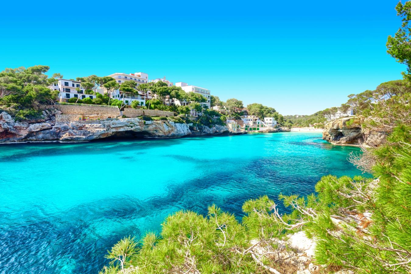 Cala Santanyí med klart turkost vatten, klippor och bebyggelse runt viken