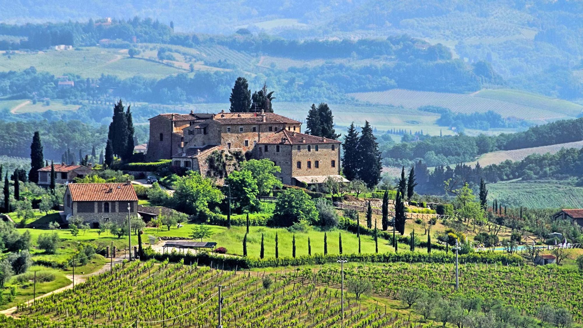 Gammel autentisk stengård i Toscana omgivet af grønne vinmarker.