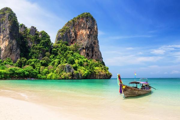 En rolig strand med båt i Phuket i Thailand, med grønnkledde klippevegger i bakgrunnen