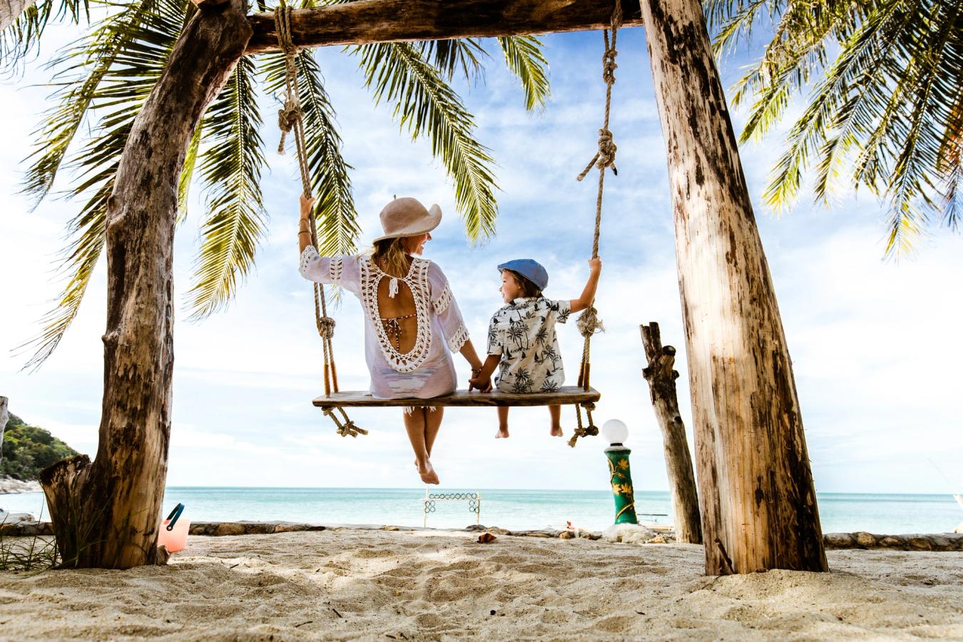 Mor och barn kopplar av under palmerna på den vita sandstranden i Thailand