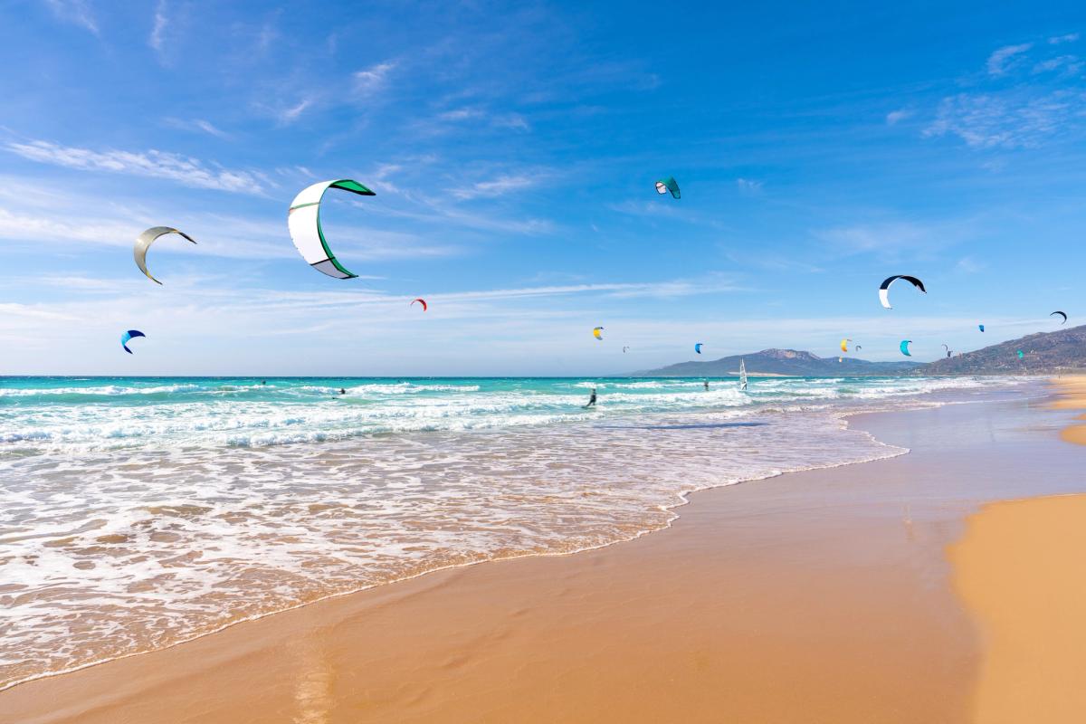 Billedet viser den populære Tarifa Beach på Costa de la Luz. Stranden er særlig populær blandt surfere og kitesurfere, som på billedet ses i fuld aktivitet.