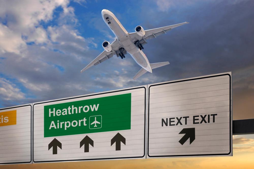Bildet viser veiskilt til Heathrow Lufthavn hvor man ser et stigende fly mot en mørk blå himmel