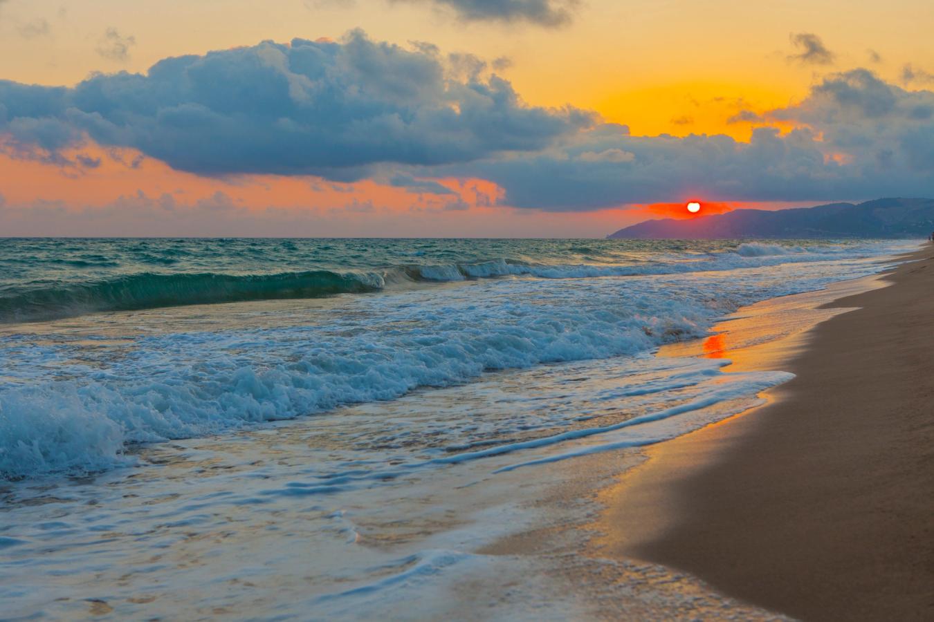 Stranden i Castelldefels med bølger som skvulper og solnedgang over horisonten